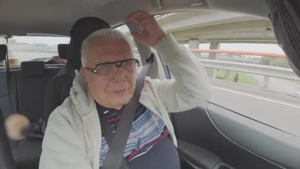 Grå-hår mand kører bil og sætter på hætte kabine udsigt – Stock-video