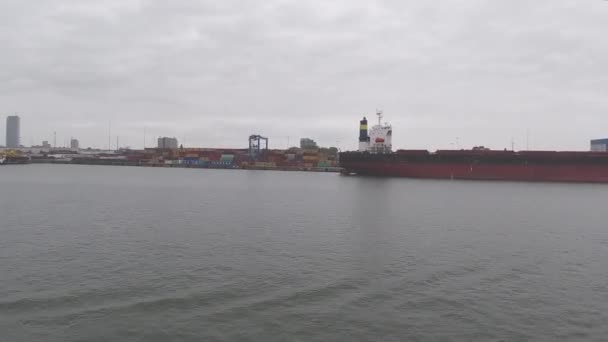 Ship sails past lighthouse yachts boats and port facilities — Stock Video