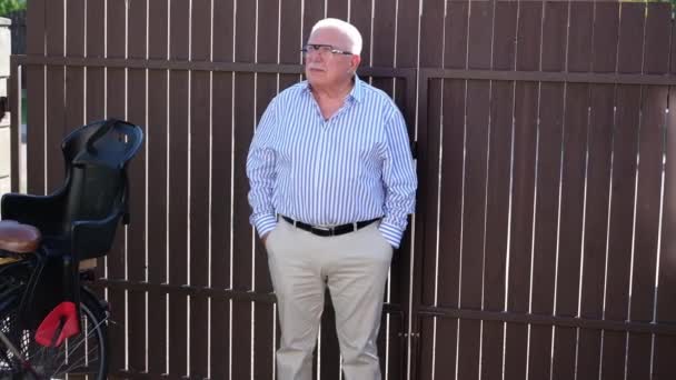 Elegante man in gestreept shirt spreekt tegen bruin hek — Stockvideo