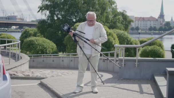 Man installs camera tripod against trees and old town tower — Stock Video