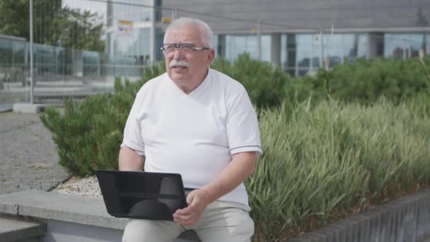 Senior man sitter på bänk och typer meddelande i laptop — Stockvideo