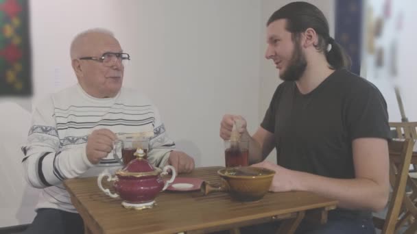 Emeryt i młodzieniec rozmawiają i parzą herbatę w miejskiej kawiarni — Wideo stockowe