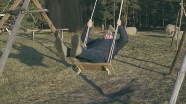 L'homme roche sur des balançoires tenant des cordes contre la forêt verte Séquence Vidéo