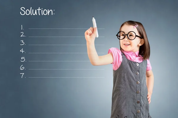 Linda niña con vestido de negocios y escribir lista de soluciones en blanco. Fondo azul . —  Fotos de Stock