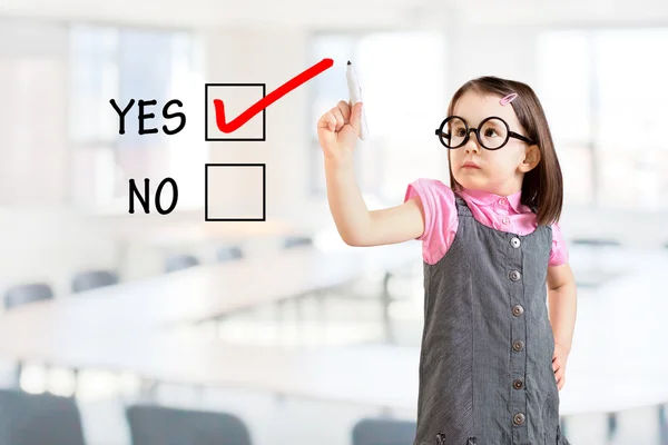 Cute little girl wearing business dress and drawing YES in a whiteboard. Office background. — Stock Photo, Image