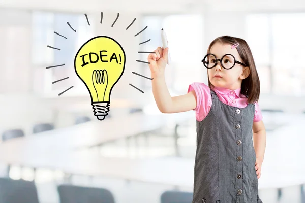 Cute little girl wearing business dress and drawing a light bulb. Office background. — Stock Photo, Image