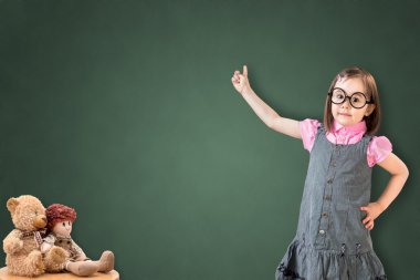 Sevimli küçük kız iş elbisesi giyen ve yeşil tebeşir tahtası üzerinde bir şey göstermek.