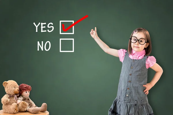 Carino bambina che indossa abito da lavoro e mostrando SI su tavola di gesso verde . — Foto Stock