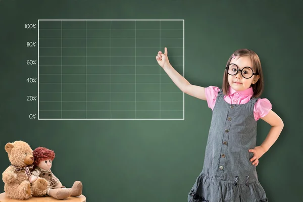 Χαριτωμένο κοριτσάκι που φοράει φόρεμα επιχειρήσεων και δείχνει στο κενό γράφημα στον πίνακα κιμωλίας πράσινο. — Φωτογραφία Αρχείου