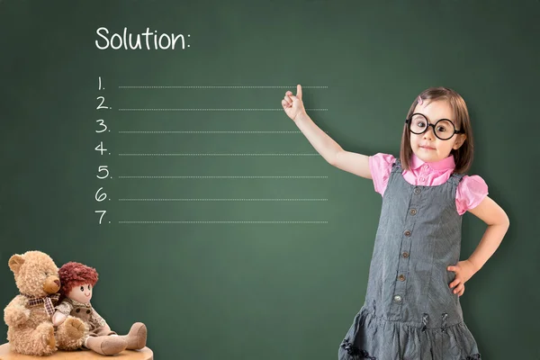 Petite fille mignonne portant une robe d'affaires et montrant la liste des solutions vierges sur le tableau de craie verte . — Photo