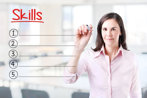 Business woman writing blank Skills list. Office background. — Stock Photo, Image