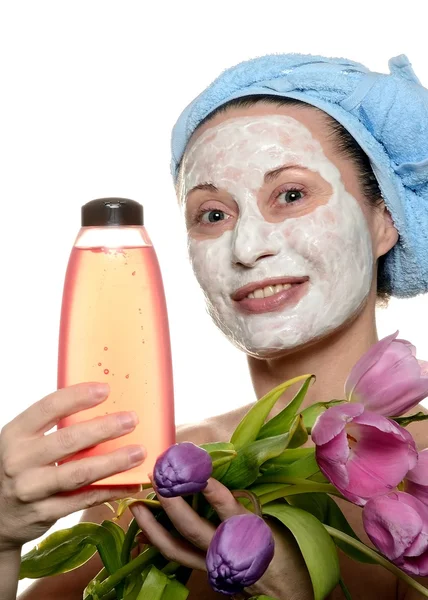 Mulher de meia-idade com uma máscara cosmética para a beleza uma pele de cara nas mãos com uma flor e pequena garrafa — Fotografia de Stock