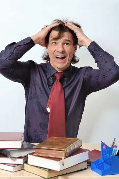 Tired scientist teacher furious among the books at table — Stock Photo, Image