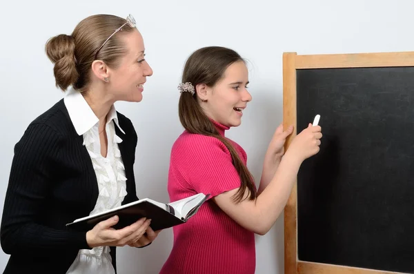 Profesora y colegiala adolescente escribiendo en pizarra escolar con tiza —  Fotos de Stock