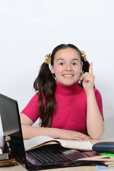 Vrolijke schattig schoolmeisje tiener aan een school Bureau lacht, houden een vinger omhoog — Stockfoto