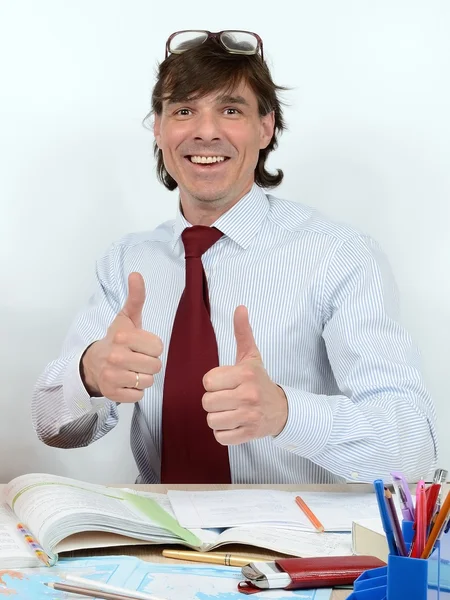 Ευτυχισμένος αρσενικό δάσκαλο στο γραφείο του, χαμογελαστό, ευχαριστημένος, δείχνει καλή τύχη — Φωτογραφία Αρχείου