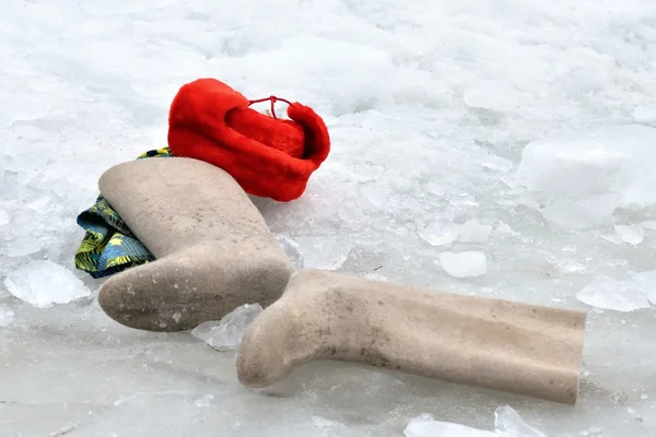 Kläder: kändes stövlar, varm röd hatt liggande på vit snö — Stockfoto