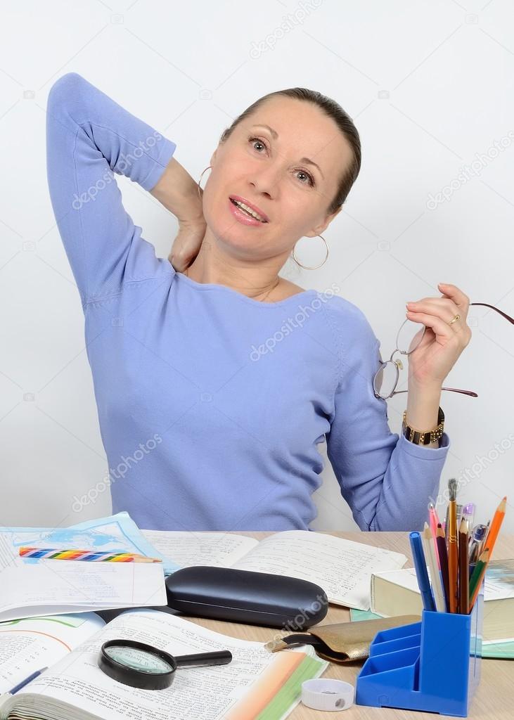 Weary woman behind the work desk kneads neck and ease back, removed his glasses be sipped