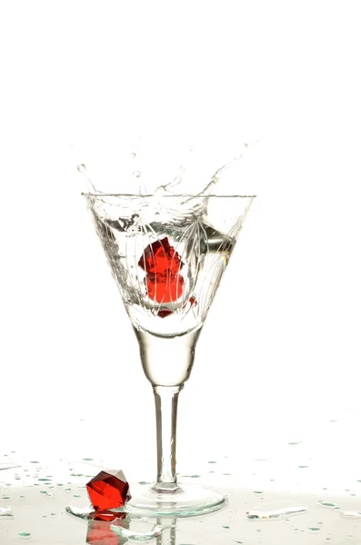 Wineglass with transparent clear water and red crystal a falling into a liquid spattering drops in different directions — Stock Photo, Image