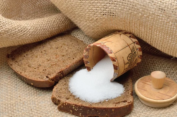 Pieces of of rye brown bread sprinkled with salt from inverted salt shakers made of birch bark on sackcloth — Stock Photo, Image