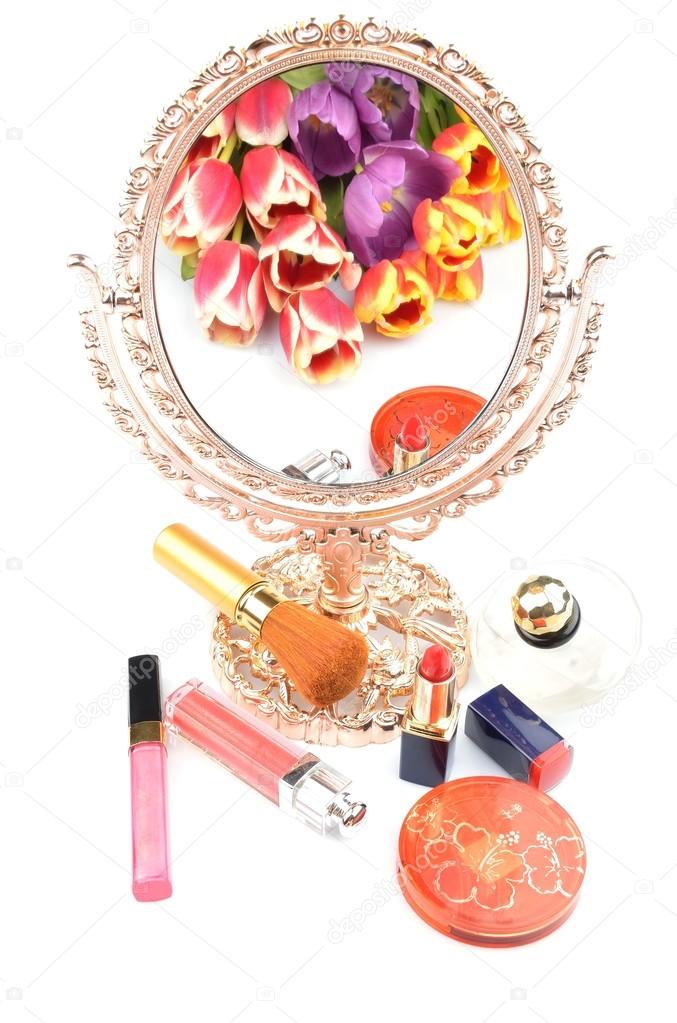 Antique gilded mirror reflecting a bouquet of flowers tulips and women's cosmetics and makeup on a white background
