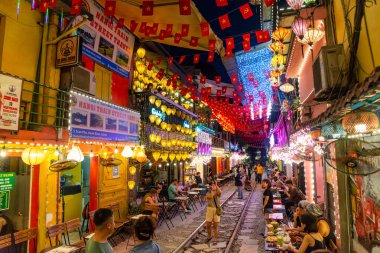 Turistler ve yerliler, Hanoi 'nin ünlü tren yolu boyunca kahve ve içkinin keyfini çıkarıyorlar. Renkli ışıklar ve şenlikli bir dekor ile parlıyorlar..