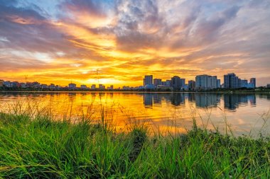 Cau Giay Park Gölü üzerinde nefes kesici bir günbatımı. Canlı bulutlar ve modern Hanoi silueti sakin suları yansıtıyor.