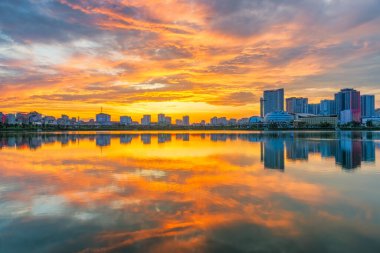 Cau Giay Park Gölü üzerinde nefes kesici bir günbatımı. Canlı bulutlar ve modern Hanoi silueti sakin suları yansıtıyor.
