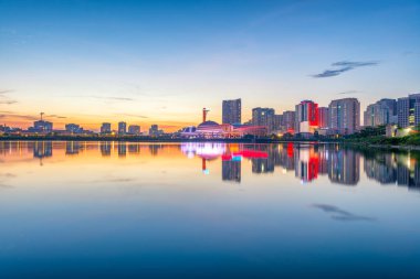Canlı bir günbatımı Hanoi 'deki Cau Giay Gölü Parkı boyunca yansıyor. Huzurlu suyu, modern gökyüzünü ve parlayan şehir ışıklarını gösteriyor.
