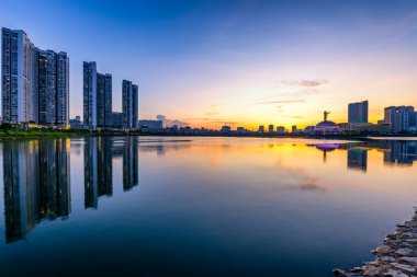 Canlı bir günbatımı Hanoi 'deki Cau Giay Gölü Parkı boyunca yansıyor. Huzurlu suyu, modern gökyüzünü ve parlayan şehir ışıklarını gösteriyor.