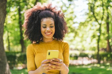 Bahçede cep telefonuyla yazı yazan güzel afro bir kadın..
