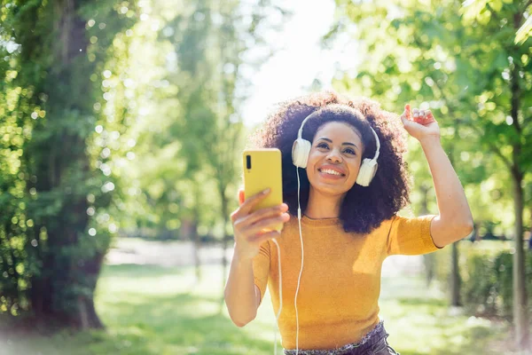 Mujer bastante afro escucha música con auriculares en un jardín. —  Fotos de Stock