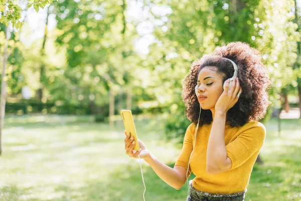 Mujer bastante afro escucha música con auriculares en un jardín. —  Fotos de Stock