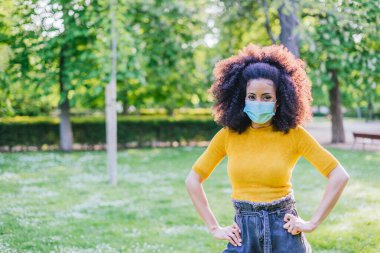 Bahçede yüzü maskeli güzel bir afro kadın gülümsüyor..