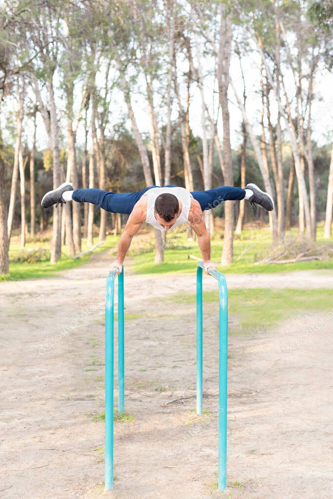 Male athlete exercising on parallel bars in forest.