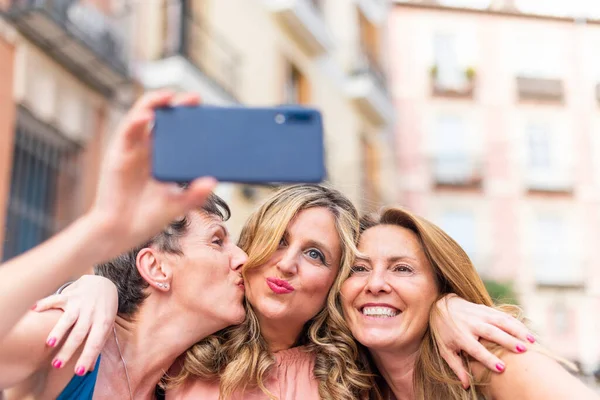 Olgun bir kadın arkadaşını yanağından öpüyor ve selfie çekiyor.