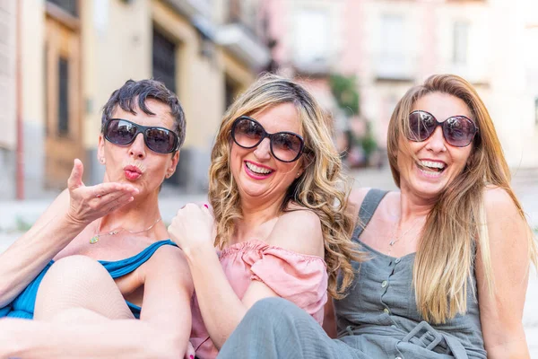 Three cheerful mature female friends with sunglasses laughing and blowing kisses — Stock Photo, Image