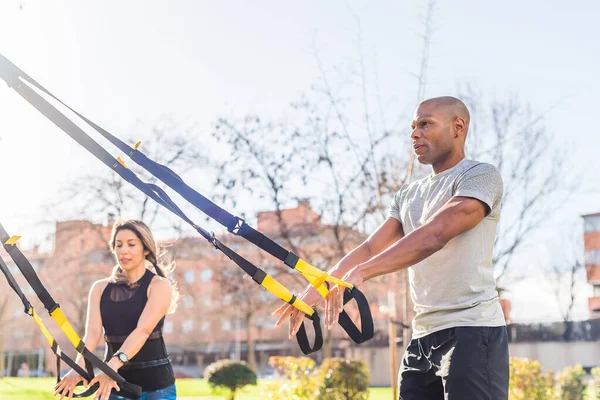 Pareja de atletas haciendo ejercicio con correas de fitness trx en el parque —  Fotos de Stock