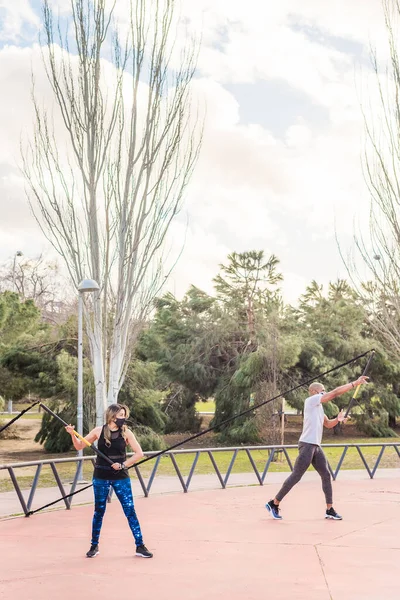 Pareja de fitness haciendo ejercicio con una correa de fitness trx en el parque. —  Fotos de Stock