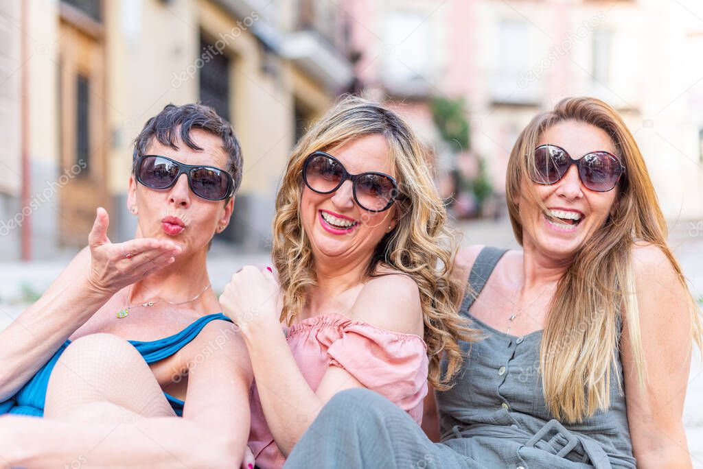 Three cheerful mature female friends with sunglasses laughing and blowing kisses