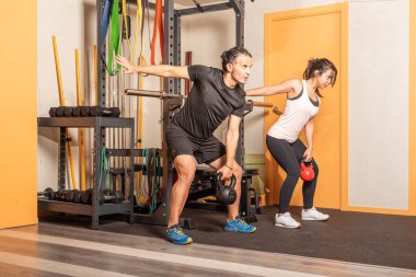 Woman and man doing shoulder press exercises with kettlebells in gym.