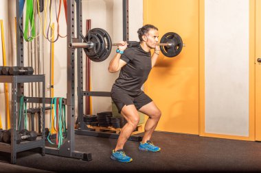 Athlete adult man doing squats with bar at gym