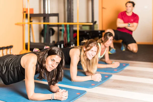 Women looking at camera doing plank exercise in the gym — Stockfoto