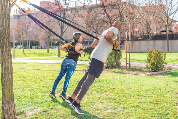 Pareja atlética haciendo ejercicio de espalda con correas de fitness en parque —  Fotos de Stock