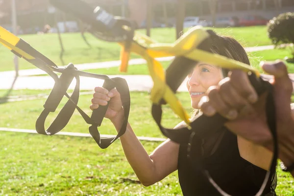 Mujer fitness haciendo ejercicio con correas de fitness en el parque — Foto de Stock