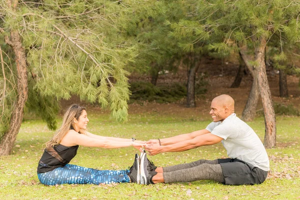 Pareja deportiva haciendo ejercicios juntos mientras están sentados y tomados de la mano —  Fotos de Stock