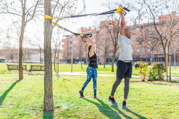 Pareja haciendo ejercicio con los brazos hacia arriba y girando el cuerpo con correas de fitness. — Foto de Stock