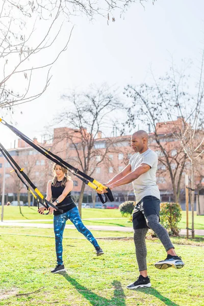 Pareja de fitness haciendo ejercicio piernas con correas de fitness en el parque — Foto de Stock