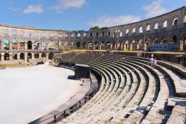 Turistler mavi gökyüzünün altında antik Roma taşından amfi tiyatroları ve dış duvarları keşfediyorlar.