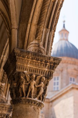 Dubrovnik, Hırvatistan, 16 Ağustos 2024. Taştan sütun sermayesi oyulmuş meleklerle ve kemerli bir tavanla, arka planda şehir mimarisi
